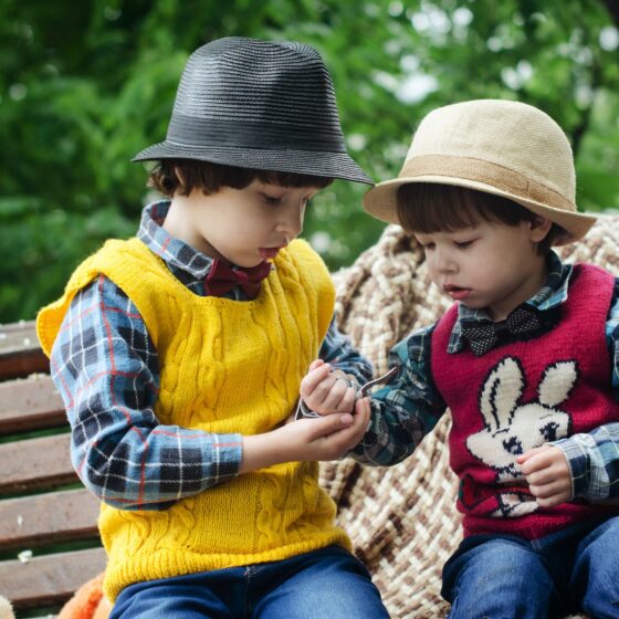 two boys sitting on bench wearing hats and long sleeved shirts
