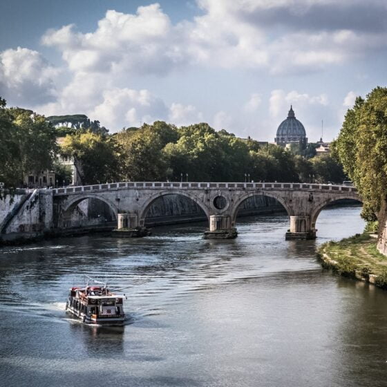 white boat on body of water crossing a gray concrete bridge during daytime. Rome Italy