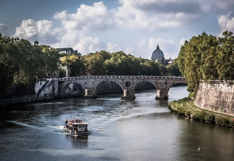 white boat on body of water crossing a gray concrete bridge during daytime. Rome Italy