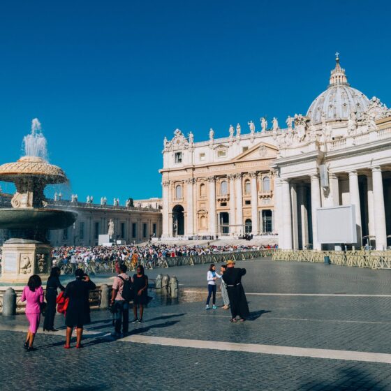 white building and people standing near water fountain at St Peter's basilica in Rome