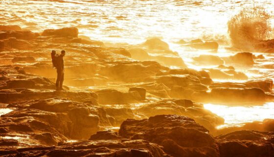 man standing on rocky shore during sunset
