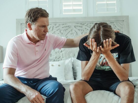 man in a pink shirt sitting beside a teenager crying