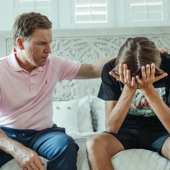 man in a pink shirt sitting beside a teenager crying