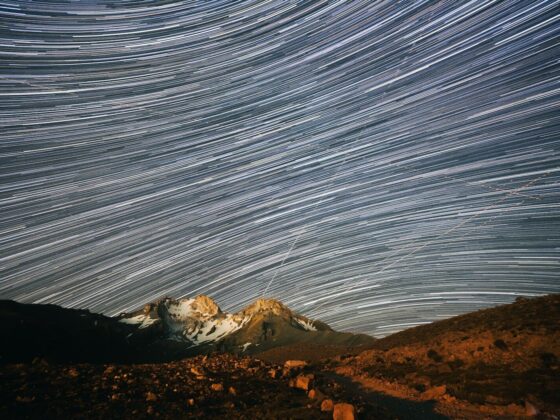 Long exposure star trails over a snow-capped mountain peak at night