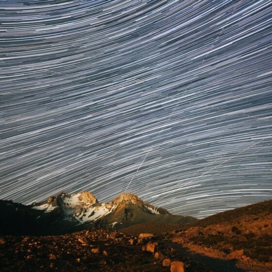 Long exposure star trails over a snow-capped mountain peak at night