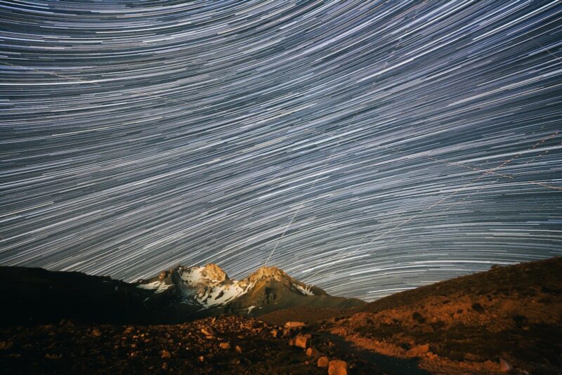 Long exposure star trails over a snow-capped mountain peak at night