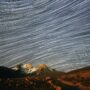 Long exposure star trails over a snow-capped mountain peak at night