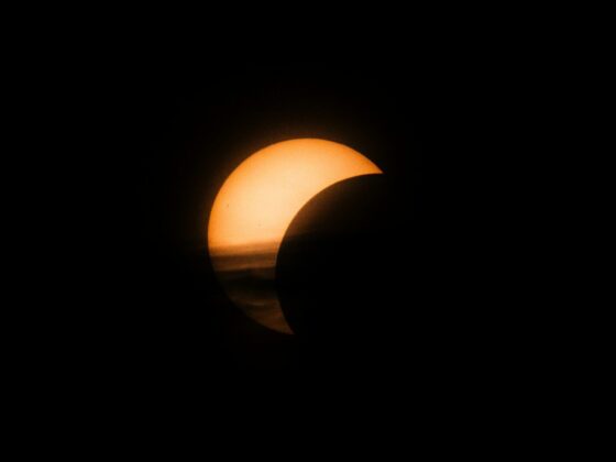 A partial solar eclipse with a glowing crescent sun against a dark sky.