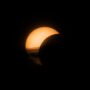 A partial solar eclipse with a glowing crescent sun against a dark sky.